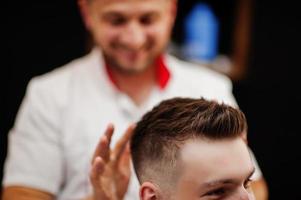 giovane uomo barbuto che si fa tagliare i capelli dal parrucchiere mentre è seduto su una sedia al barbiere. anima da barbiere. foto