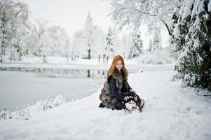 ragazza dai capelli rossi che cammina al parco con un cane husky il giorno d'inverno. foto