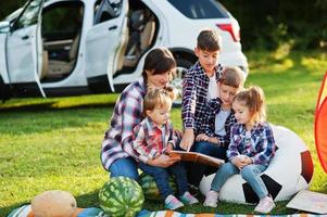 famiglia che trascorre del tempo insieme. libro di lettura della madre all'aperto con i bambini contro la loro auto suv. foto