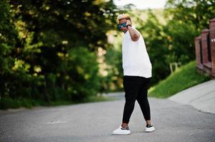 elegante ragazzo musulmano arabo con originariamente capelli e occhiali da sole in posa per le strade. foto