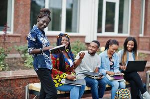 gruppo di cinque studenti universitari africani che trascorrono del tempo insieme nel campus nel cortile dell'università. amici afro neri che studiano al banco con articoli per la scuola, notebook portatili. foto