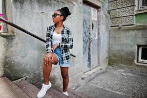 ragazza afroamericana hip hop su occhiali da sole e pantaloncini di jeans. ritratto di moda di strada casual di donna nera. foto