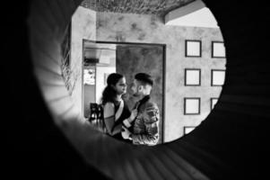 adorabile coppia indiana innamorata, indossata a saree e abito elegante, posata sul ristorante al cerchio rotondo al muro. foto