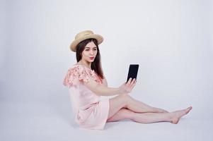 ritratto di una donna alla moda in abito rosa e cappello seduta sul pavimento e facendo selfie in studio. foto