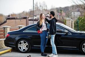 bella coppia multirazziale abbraccia insieme contro un'elegante auto sportiva nera. foto