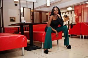 bellezza sottile modello afroamericano indossare su camicetta nera e pantaloni verdi gambe lunghe poste al caffè cinese. foto