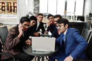 gruppo di sei uomini d'affari indiani in giacca e cravatta seduti in ufficio al bar e guardando il computer portatile. foto