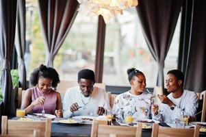 felici amici africani seduti, chiacchierando al bar e mangiando cibo. gruppo di persone di colore che si incontrano al ristorante e cenano. foto