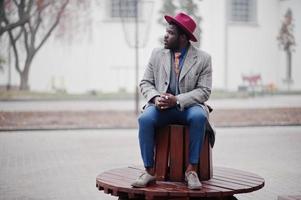 elegante modello uomo afroamericano in cappotto grigio, cravatta giacca e cappello rosso. foto