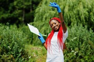 donna volontaria dai capelli rossi africana con appunti nel parco. concetto di volontariato, carità, persone ed ecologia in africa. foto