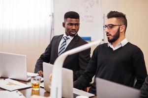 team aziendale multirazziale che si rivolge alla riunione attorno al tavolo della sala riunioni. uomo d'affari africano e arabo. foto