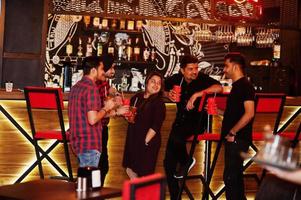 gruppo di amici indiani che si divertono e riposano al night club, bevendo cocktail vicino al bancone del bar. foto