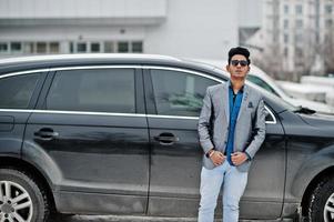 casual giovane indiano in occhiali da sole poste contro l'auto suv. foto