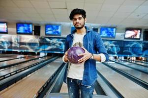 uomo asiatico con barba alla moda in camicia di jeans in piedi alla pista da bowling con palla a portata di mano. foto