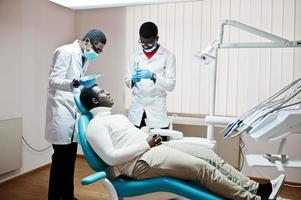 paziente uomo afroamericano in poltrona odontoiatrica. studio dentistico e concetto di pratica medica. dentista professionista che aiuta il suo paziente in odontoiatria medica. anestetico per iniezione. foto