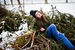 la ragazza indossa una lunga felpa verde, jeans e copricapo nero sui rami del pino nelle giornate invernali. foto