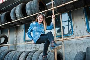 giovane ragazza hipster in giacca di jeans e sciarpa per la testa nella zona di montaggio dei pneumatici. foto