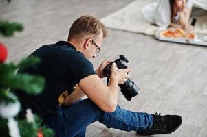 fotografo uomo spara su ragazze gemelle in studio che stanno mangiando pizza. fotografo professionista al lavoro. foto