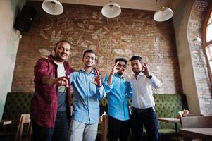 un gruppo di quattro uomini del sud asiatico poste alla riunione di lavoro nella caffetteria. indiani che conversano e mostrano segni di ok. foto
