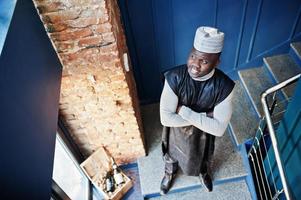 vista dall'alto dell'uomo africano in abiti tradizionali neri con cappuccio posato al ristorante sulle scale. foto