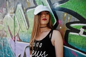 ragazza hipster casual alla moda in berretto e jeans indossano contro un grande muro di graffiti. foto