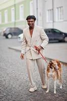 elegante uomo afro in abito beige vecchia scuola con cane borzoi russo. giovane maschio africano alla moda in giacca casual sul torso nudo. foto