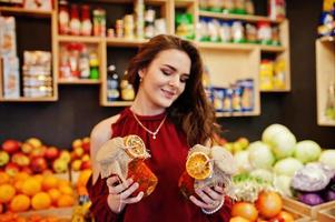 ragazza in rosso che tiene marmellata in un barattolo sul negozio di frutta. foto