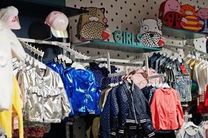 i vestiti luminosi per bambini sono appesi sul display nel negozio di abbigliamento per bambini. sezione ragazze. foto
