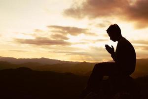la sagoma di un uomo sta pregando Dio sulla montagna. mani in preghiera, rispetto. foto