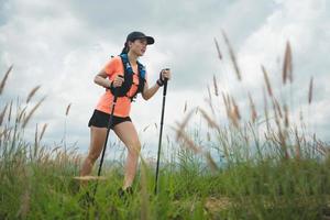 giovani donne sentiero attivo che corre attraverso un prato su un sentiero erboso in alta montagna nel pomeriggio con palo da trekking foto