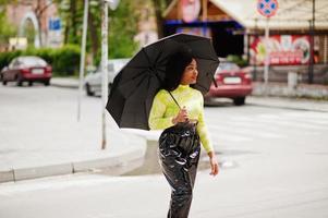 ritratto di giovane bella donna afroamericana con ombrello nero e attraversamento pedonale a piedi. foto