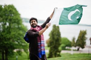 l'uomo pakistano indossa abiti tradizionali e tiene la bandiera del pakistan. foto