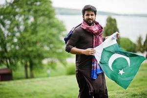 l'uomo pakistano indossa abiti tradizionali e tiene la bandiera del pakistan. foto