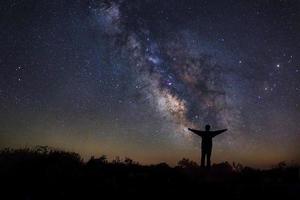 paesaggio con via lattea, cielo notturno con stelle e silhouette di un uomo felice in piedi sulla montagna, fotografia a lunga esposizione, con grano foto