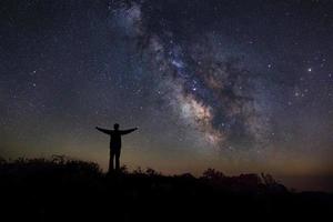 paesaggio con via lattea, cielo notturno con stelle e silhouette di un uomo felice in piedi sulla montagna, fotografia a lunga esposizione, con grano foto