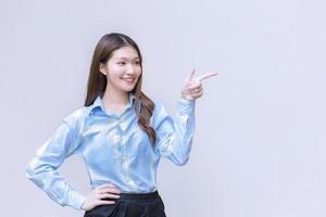 la donna asiatica che lavora con i capelli lunghi che indossa una camicia blu a maniche lunghe sorride felicemente mentre mostra il punto per presentare qualcosa su sfondo bianco. foto