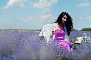 bella ragazza indiana indossa un abito tradizionale indiano saree seduto in un campo di lavanda viola con decorazioni. foto