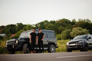 due fratelli asiatici indossano un uomo tutto nero in posa vicino alle auto suv. foto