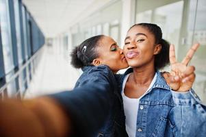 due amiche africane in giacca di jeans che fanno selfie con la fotocamera al coperto insieme. foto