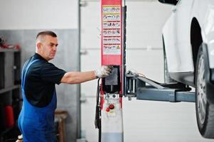 tema riparazione e manutenzione auto. meccanico in uniforme che lavora in servizio automatico, premere il pulsante per sollevare l'auto. foto