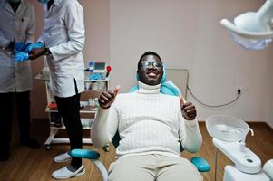 soddisfatto uomo afroamericano paziente in poltrona odontoiatrica mostra pollice in su. studio dentistico e concetto di pratica medica. foto