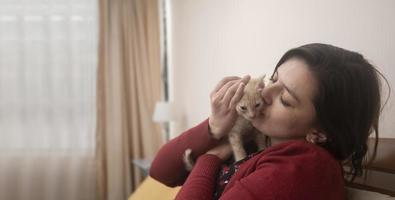 ritratto di bella donna ispanica che abbraccia e bacia il suo gattino carino all'interno della sua stanza con sfondo sfocato foto