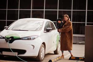 giovane madre con bambino che carica l'auto elettrica presso la stazione di servizio elettrica. foto