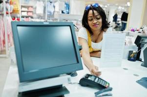 cliente donna afroamericana felice con borse della spesa colorate che pagano con carta di credito vicino a terminali in contanti con pos. foto