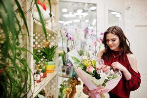 ragazza bruna in rosso comprare fiori al negozio di fiori. foto