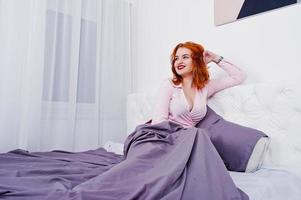ritratto di una ragazza dai capelli rossi attraente sdraiata sul letto e che si copre con una coperta viola. foto