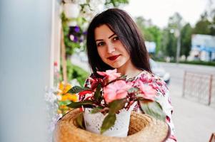 ritratto estivo di ragazza bruna con occhiali rosa e cappello contro il negozio di fiori. foto