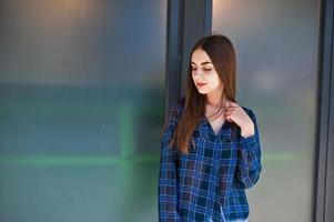 ritratto di giovane ragazza bruna in camicia a scacchi blu contro grandi finestre. foto