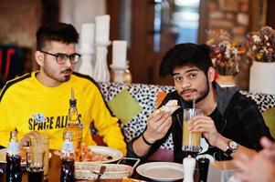 ragazzi asiatici di amici che mangiano pizza durante la festa in pizzeria. felici indiani che si divertono insieme, mangiano cibo italiano e si siedono sul divano. foto