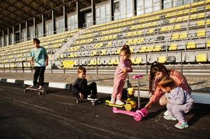 giovane madre alla moda con quattro bambini all'aperto. la famiglia sportiva trascorre il tempo libero all'aria aperta con scooter e pattini. dipinto con il gesso sull'asfalto. foto